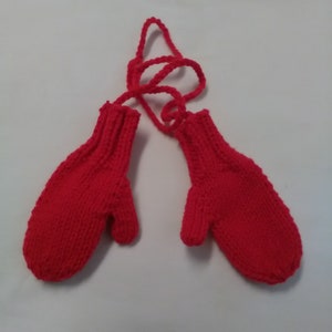 May include: A pair of red knitted mittens with a long tie string. The mittens are made of a soft, warm yarn and have a simple, classic design.