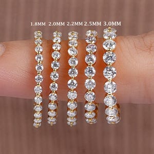 Könnte beinhalten: Eine Auswahl goldfarbener Ringe, jeweils mit klaren, funkelnden Edelsteinen besetzt. Die Ringe sind in verschiedenen Größen erhältlich, von 1,8 mm bis 3,0 mm, mit dem Text "1.8MM 2.0MM 2.2MM 2.5MM 3.0MM" darüber. Gezeigt auf einem Finger.