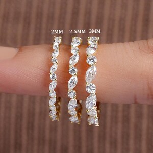May include: Three gold rings with clear gemstones are shown. The rings are labelled with sizes: 2mm, 2.5mm, and 3mm. The gemstones are set in a repeating pattern along the bands, creating a sparkling effect.
