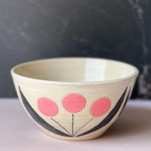 A white ceramic bowl with a floral design featuring three pink flowers and black stems.