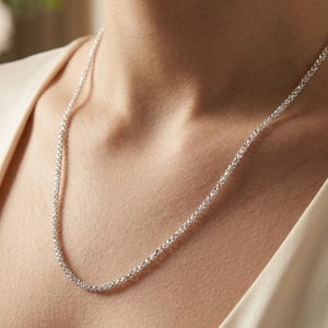 Op de afbeelding: Een delicate zilveren ketting met een getextureerd, kralenontwerp. De ketting is om de nek gedrapeerd, waardoor een eenvoudige maar elegante uitstraling ontstaat. De achtergrond is een zachte, neutrale kleur, die de sieraden benadrukt.