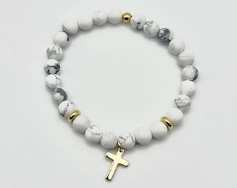 Op de afbeelding: Armband met witte en grijze gemarmerde kralen, gouden afstandhouders en een gouden kruisbedel. De kralen zijn rond en het kruis hangt in het midden. Een religieus sieraad.