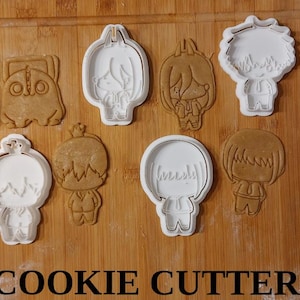 Peut inclure: Diverses découpoirs à biscuits en forme de personnages, blancs et bruns, disposés sur une surface en bois. Le texte "COOKIE CUTTER" est imprimé en noir en bas de l'image. Idéal pour la pâtisserie créative.