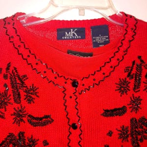 May include: A vibrant red cardigan with black beaded detailing and a zig-zag trim. The sweater features black buttons and a label reading "MK Sweaters". The size is small.