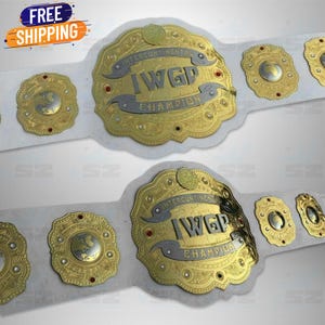 Könnte beinhalten: Zwei gold-silberne Intercontinental IWGP Champion Wrestling-Gürtel mit weißen Riemen. Die Gürtel haben aufwendige Designs und die Worte "INTERCONTINENTAL IWGP CHAMPION" sind sichtbar. Das Bild enthält auch ein "FREE SHIPPING" Banner.