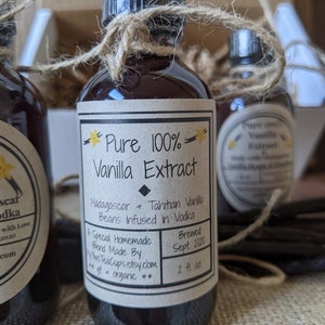 May include: A glass bottle of pure vanilla extract with a brown label that reads "Pure 100% Vanilla Extract" and "Madagascar & Tahitian Vanilla Beans Infused in Vodka". The label also includes the text "Brewed Sept 2020" and "2 fl oz".