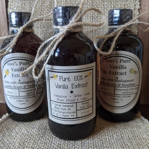 May include: Three glass bottles of pure vanilla extract, each with a different label. The center bottle is labeled "Pure 100% Vanilla Extract" with the text "Madagascar + Tahitian Vanilla Beans Infused in Vodka". The bottle on the left is labeled "100% Pure Vanilla Extract" with the text "Made with Madagascar Vanilla Beans & Vodka". The bottle on the right is labeled "100% Pure Vanilla Extract" with the text "Made with Madagascar Vanilla Beans & Bourbon".