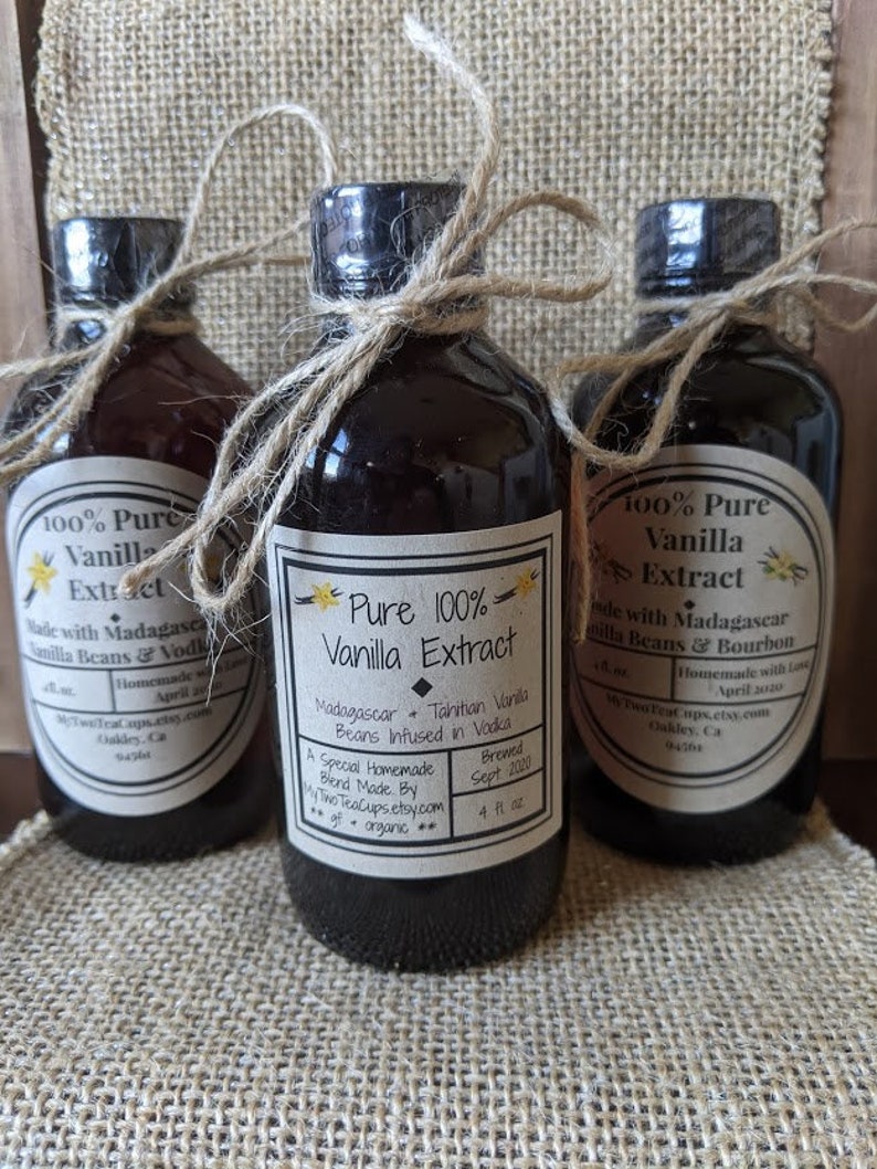 May include: Three glass bottles of pure vanilla extract, each with a different label. The center bottle is labeled "Pure 100% Vanilla Extract" with the text "Madagascar + Tahitian Vanilla Beans Infused in Vodka". The bottle on the left is labeled "100% Pure Vanilla Extract" with the text "Made with Madagascar Vanilla Beans & Vodka". The bottle on the right is labeled "100% Pure Vanilla Extract" with the text "Made with Madagascar Vanilla Beans & Bourbon".
