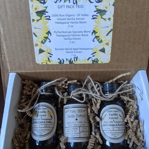 May include: A gift box set containing three 2-ounce bottles of pure vanilla extract. The bottles are labeled "Pure 100% Vanilla Extract" and list the ingredients as Madagascar vanilla beans and vodka. The box is labeled "Gift Pack Trio" and lists the three different types of vanilla extract included: "100% Pure Organic - GF Vodka - Infused Vanilla Extract Madagascar Vanilla Beans 2 oz.", "MyTwoTeaCups Specialty Blend Madagascar/Tahitian Blend Vanilla Extract 2 oz.", and "Bourbon Barrel Aged Madagascar Vanilla Extract 2 oz."