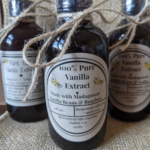 May include: Three glass bottles of 100% pure vanilla extract, made with Madagascar vanilla beans and bourbon. The bottles are tied with twine and have labels with the product name, ingredients, and contact information. The bottles are sitting on a burlap surface.