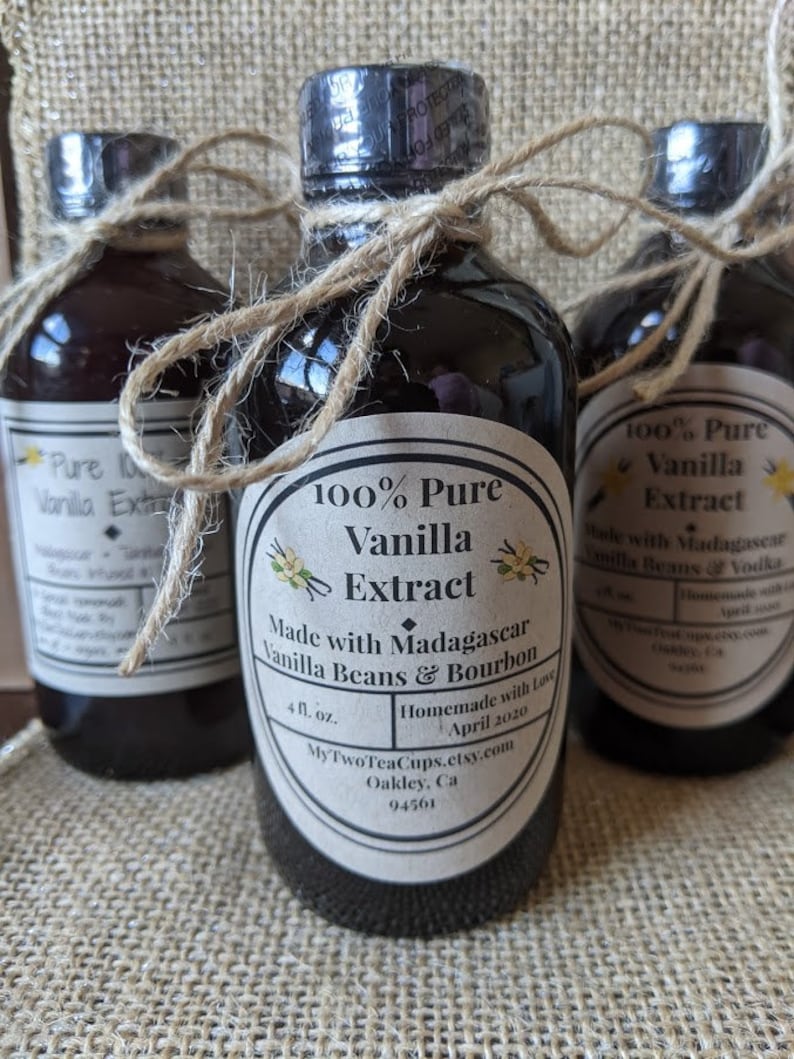 May include: Three glass bottles of 100% pure vanilla extract, made with Madagascar vanilla beans and bourbon. The bottles are tied with twine and have labels with the product name, ingredients, and contact information. The bottles are sitting on a burlap surface.