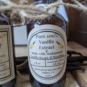 May include: A glass bottle of pure vanilla extract with a brown label that reads "Pure 100% Vanilla Extract Made with Madagascar Vanilla Beans & Bourbon 2 fl. oz. Homemade with Love July 2020 MyTwoTeaCups.etsy.com Oakley, CA 94561"