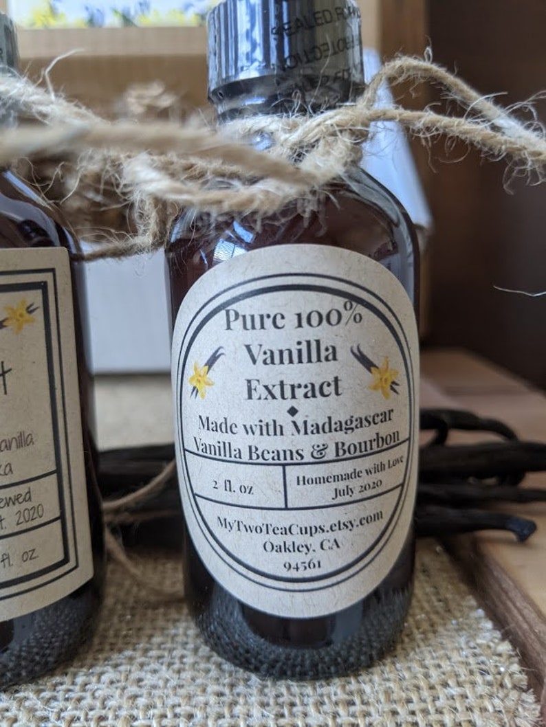 May include: A glass bottle of pure vanilla extract with a brown label that reads "Pure 100% Vanilla Extract Made with Madagascar Vanilla Beans & Bourbon 2 fl. oz. Homemade with Love July 2020 MyTwoTeaCups.etsy.com Oakley, CA 94561"