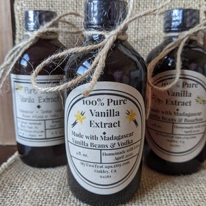May include: Three glass bottles of 100% pure vanilla extract, tied with twine. The center bottle label reads "100% Pure Vanilla Extract Made with Madagascar Vanilla Beans & Vodka Homemade with Love April 2020 MyTwoTeaCups.etsy.com Oakley, Ca 94561".