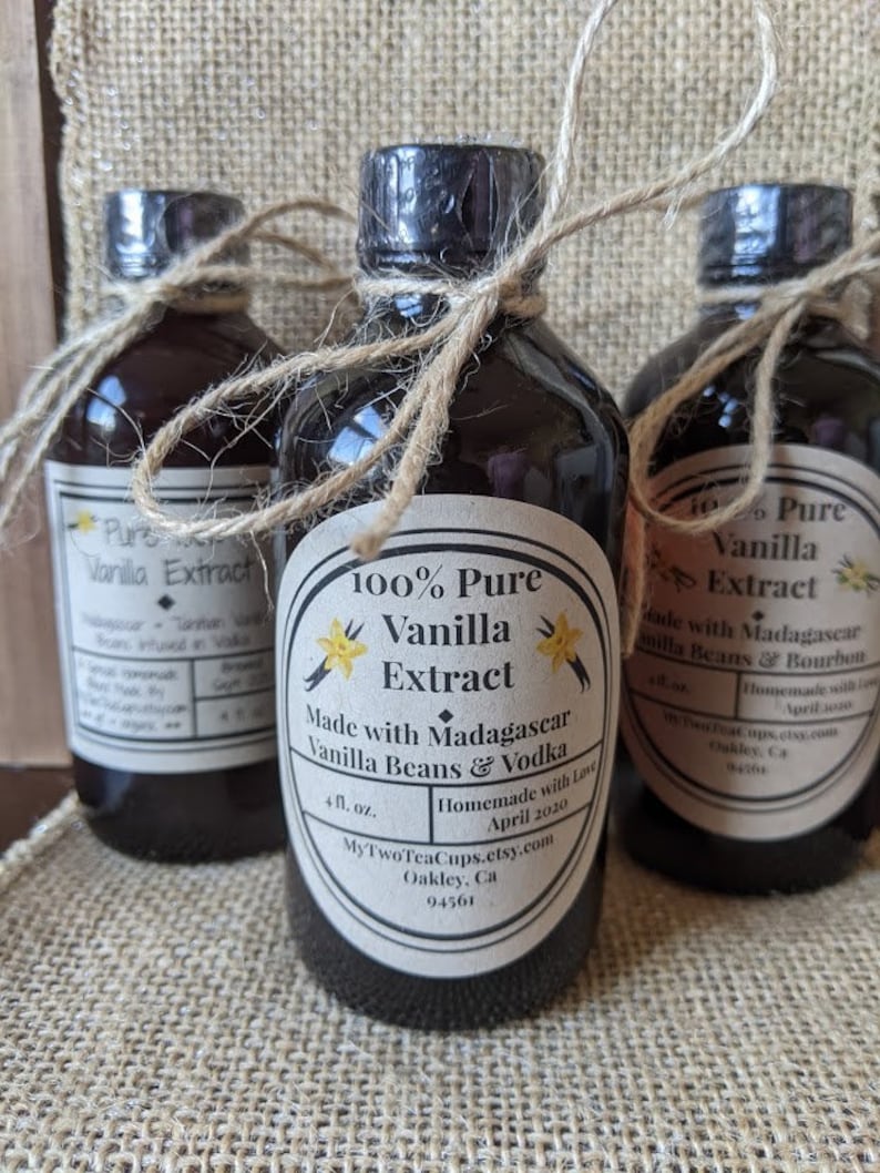 May include: Three glass bottles of 100% pure vanilla extract, tied with twine. The center bottle label reads "100% Pure Vanilla Extract Made with Madagascar Vanilla Beans & Vodka Homemade with Love April 2020 MyTwoTeaCups.etsy.com Oakley, Ca 94561".