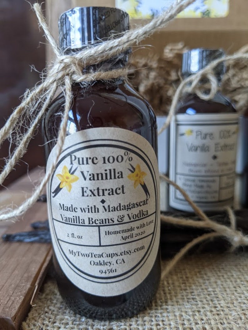 May include: A glass bottle with a brown label that reads "Pure 100% Vanilla Extract Made with Madagascar Vanilla Beans & Vodka Homemade with Love April 2020 MyTwoTeaCups.etsy.com Oakley, CA 94561". The bottle is tied with twine and has a yellow flower graphic on the label.