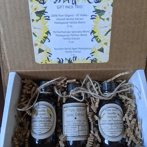 May include: A gift box set containing three 2-ounce bottles of pure vanilla extract. The bottles are labeled "Pure 100% Vanilla Extract" and list the ingredients as Madagascar vanilla beans and vodka. The box is labeled "Gift Pack Trio" and lists the three different types of vanilla extract included: "100% Pure Organic - GF Vodka - Infused Vanilla Extract Madagascar Vanilla Beans 2 oz.", "MyTwoTeaCups Specialty Blend Madagascar/Tahitian Blend Vanilla Extract 2 oz.", and "Bourbon Barrel Aged Madagascar Vanilla Extract 2 oz."