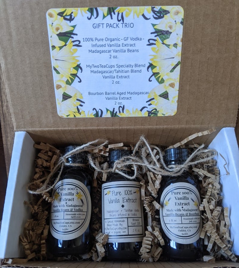 May include: A gift box set containing three 2-ounce bottles of pure vanilla extract. The bottles are labeled "Pure 100% Vanilla Extract" and list the ingredients as Madagascar vanilla beans and vodka. The box is labeled "Gift Pack Trio" and lists the three different types of vanilla extract included: "100% Pure Organic - GF Vodka - Infused Vanilla Extract Madagascar Vanilla Beans 2 oz.", "MyTwoTeaCups Specialty Blend Madagascar/Tahitian Blend Vanilla Extract 2 oz.", and "Bourbon Barrel Aged Madagascar Vanilla Extract 2 oz."