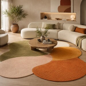Puede incluir: Un salón moderno con un gran sofá curvo de color crema, una mesa de centro redonda de madera y una alfombra multicolor. La alfombra tiene un diseño floral único con tonos de verde, melocotón, naranja y crema. Una planta en maceta y un sillón blanco completan la escena.