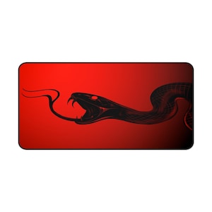 Puede incluir: Alfombrilla de ratón rectangular con un diseño de serpiente negra sobre un fondo degradado rojo. La serpiente se representa con la boca abierta, colmillos a la vista y lengua extendida. El diseño es una ilustración estilizada.