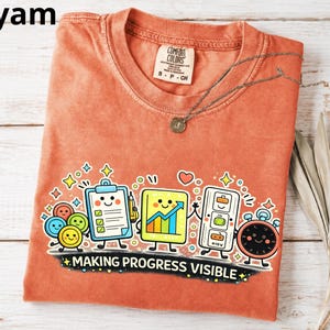 Könnte beinhalten: Ein rostorangefarbenes T-Shirt mit Rundhalsausschnitt und einem Grafikdruck von Büroartikeln mit Gesichtern, darunter ein Klemmbrett, ein Diagramm und ein Timer. Der Text "MAKING PROGRESS VISIBLE" ist in Weiß unter den Figuren gedruckt.