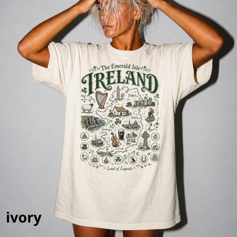 Puede incluir: Una camiseta de manga corta color marfil con un estampado gr&aacute;fico en verde y marr&oacute;n de un mapa de Irlanda. El texto dice The Emerald Isle, IRELAND y Land of Legends, rodeado de ilustraciones de un arpa, ovejas, acantilados y una pinta.