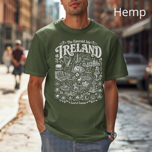Puede incluir: Una camiseta de manga corta color verde oliva con un estampado gr&aacute;fico blanco de un mapa de Irlanda. El dise&ntilde;o incluye el texto The Emerald Isle IRELAND Land of Legends, junto con ilustraciones de un arpa, tr&eacute;boles y varios monumentos.