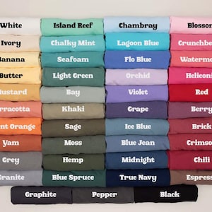 Puede incluir: Una carta de colores con cuarenta y ocho camisetas dobladas dispuestas en una cuadr&iacute;cula. Cada camiseta muestra el nombre de su color en texto negrita blanco o negro. La paleta incluye varios tonos de blanco, amarillo, naranja, verde, azul, morado, rosa, rojo, marr&oacute;n, gris y negro.