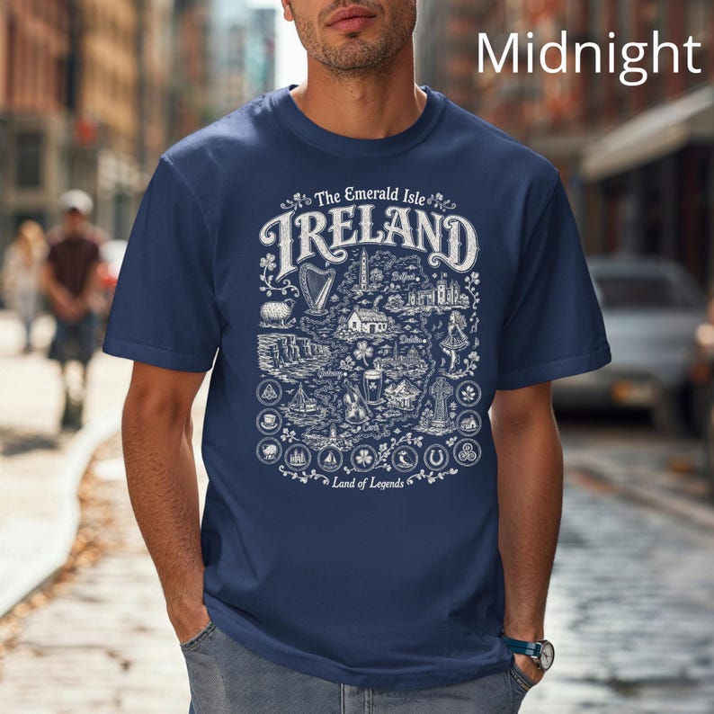 Puede incluir: Una camiseta azul marino de manga corta con un estampado gr&aacute;fico blanco de un mapa de Irlanda. El dise&ntilde;o incluye el texto The Emerald Isle IRELAND Land of Legends, junto con ilustraciones de un arpa, tr&eacute;boles y varios puntos de referencia.