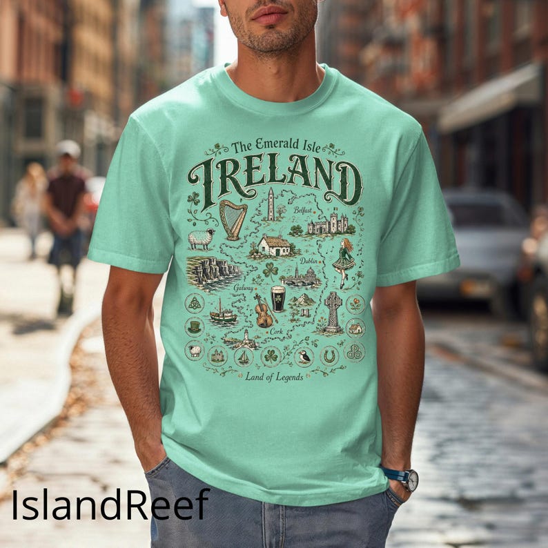 Puede incluir: Una camiseta de color verde menta claro con un mapa gr&aacute;fico detallado de Irlanda. El dise&ntilde;o incluye el texto The Emerald Isle IRELAND Land of Legends, junto con ilustraciones de un arpa, ovejas, acantilados, un viol&iacute;n y una cruz celta.