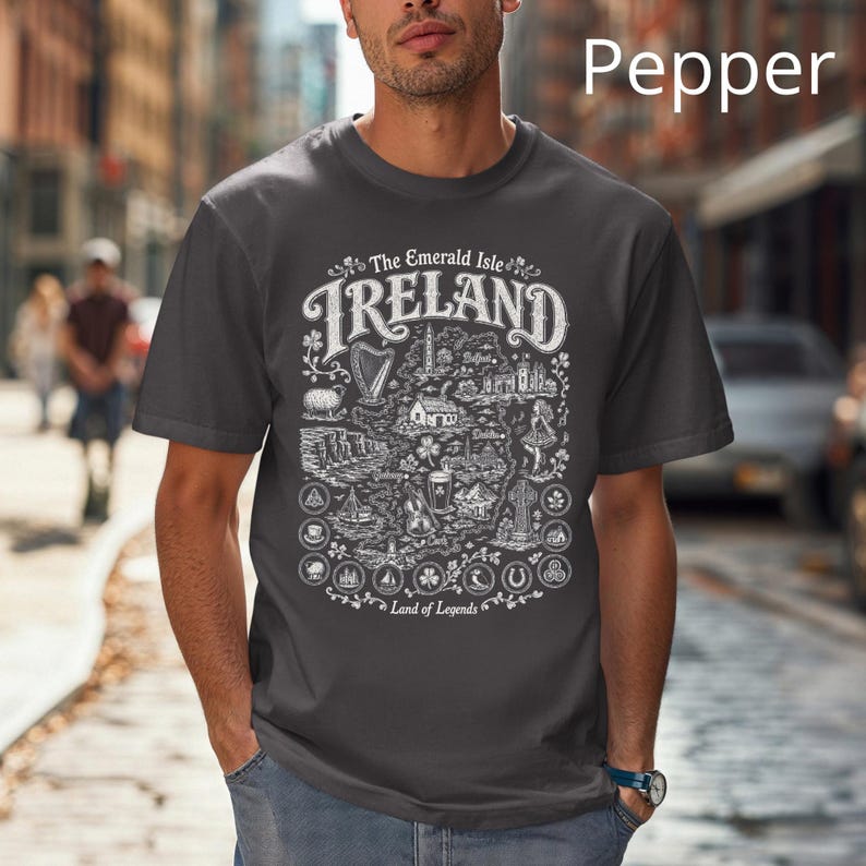 Puede incluir: Una camiseta gris carb&oacute;n con un estampado gr&aacute;fico blanco de un mapa de Irlanda. El dise&ntilde;o incluye el texto The Emerald Isle, IRELAND y Land of Legends, junto con ilustraciones de un arpa, una oveja, acantilados, una pinta y una cruz celta.