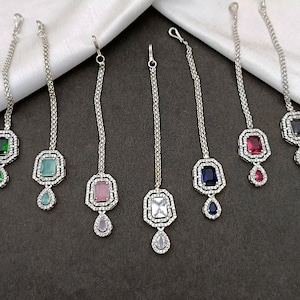 May include: A selection of silver-coloured headpieces, each featuring a central rectangular gemstone in colours such as green, blue, pink, red, and clear. Each piece has a chain and a teardrop-shaped gem.