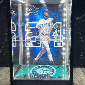 May include: A lit display case featuring a baseball player in a Seattle Mariners uniform. The case has a black frame and a green and blue baseball field design at the base. The player's image is surrounded by a blue and white background.