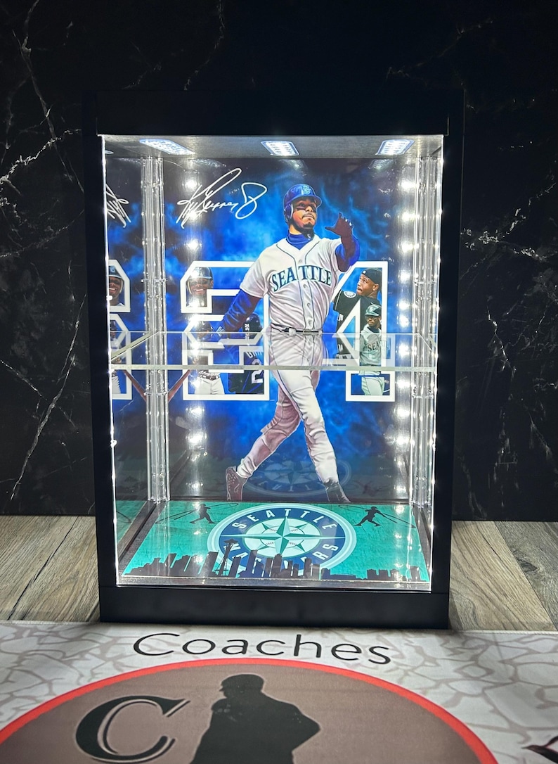 May include: A black display case featuring a baseball player image, lit by internal lights. The player is in a Seattle Mariners uniform. The case has a green and blue base with the team logo. The player's signature is visible.