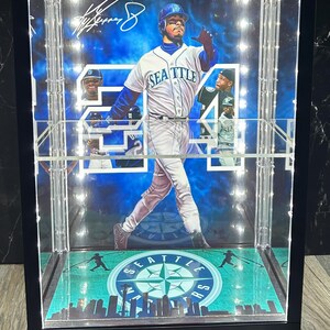 May include: A framed baseball display featuring a player in a Seattle Mariners uniform. The display includes the number 24, the team logo, and a signature. The background is a blue sky with clouds. The display case has a black frame.