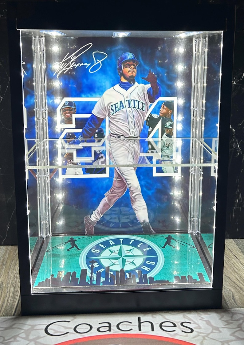 May include: A framed baseball display featuring a player in a Seattle Mariners uniform. The display includes the number 24, the team logo, and a signature. The background is a blue sky with clouds. The display case has a black frame.
