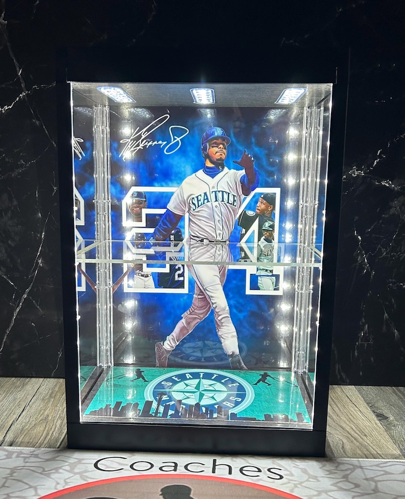 May include: A display case featuring a baseball player in a Seattle Mariners uniform. The case has a black frame, a clear front, and is illuminated with LED lights. The player's signature is visible. The base of the case has a green and blue design.