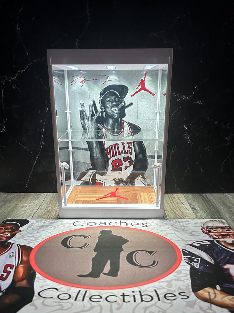 May include: A white display case featuring a black and white image of Michael Jordan in a Chicago Bulls jersey. The case has a wooden floor with a red Jumpman logo. Red accents and a Jumpman logo are visible.