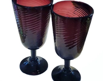 May include: Two purple glass wine glasses with a swirl pattern. The glasses have black stems and bases.