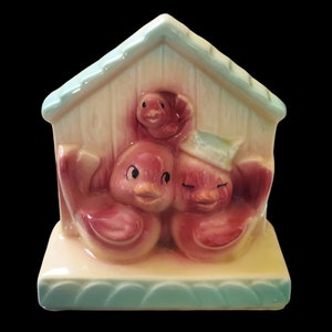 May include: A ceramic birdhouse planter with three pink birds. The birdhouse is painted in shades of yellow and green. The birds are peeking out of the birdhouse.