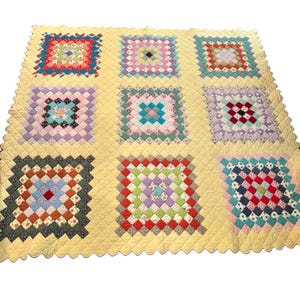 May include: A quilt featuring a pale yellow background with a scalloped edge and nine large square blocks. Each block is composed of smaller, multi-colored fabric squares arranged in a concentric pattern, showcasing various floral and geometric prints.