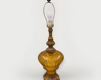 May include: An antique table lamp with a golden-amber glass shade and ornate bronze base. The lamp features a decorative finial and a curved metal support for the lightbulb. The lamp is approximately 28 inches tall.