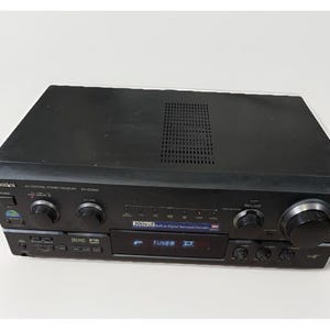 Pode incluir: Receptor estéreo de controle AV preto com vários botões e botões. O receptor possui um display digital que lê "TUNER". O número do modelo é SA-DX940. O receptor possui um decodificador surround digital integrado.