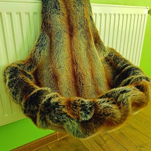 Könnte beinhalten: Ein Haustierbett aus Kunstfell in Braun-, Schwarz- und Beigetönen. Das Bett hat eine kreisförmige Form mit einem erhöhten Rand und einem weichen, plüschigen Innenraum. Das Bett soll einem kleinen Haustier Komfort und Wärme bieten.