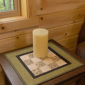 K&ouml;nnte beinhalten: Eine cremefarbene S&auml;ulenkerze auf einem dunklen Holzbeistelltisch. Der Tisch hat eine quadratische, gesteppte Tischdecke mit gr&uuml;nem Rand und einem gemusterten Mittelteil. Der Hintergrund zeigt ein Fenster und Holzverkleidungen.