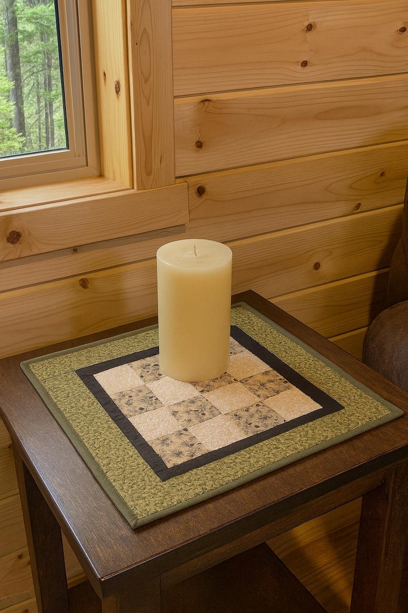 K&ouml;nnte beinhalten: Eine cremefarbene S&auml;ulenkerze auf einem dunklen Holzbeistelltisch. Der Tisch hat eine quadratische, gesteppte Tischdecke mit gr&uuml;nem Rand und einem gemusterten Mittelteil. Der Hintergrund zeigt ein Fenster und Holzverkleidungen.