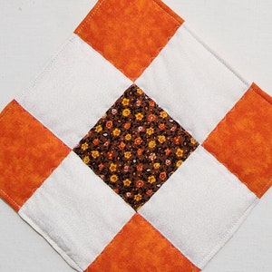 Get into the season with handmade quilted potholders. Perfect fall colors: orange, white and brown floral nine patch quilted trivets