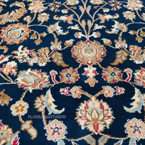 May include: Close-up of a navy blue rug with an intricate floral pattern. The design features beige, red, and light blue floral motifs and scrolling vines. The text "FLORALRUGSTOREIN" is visible.