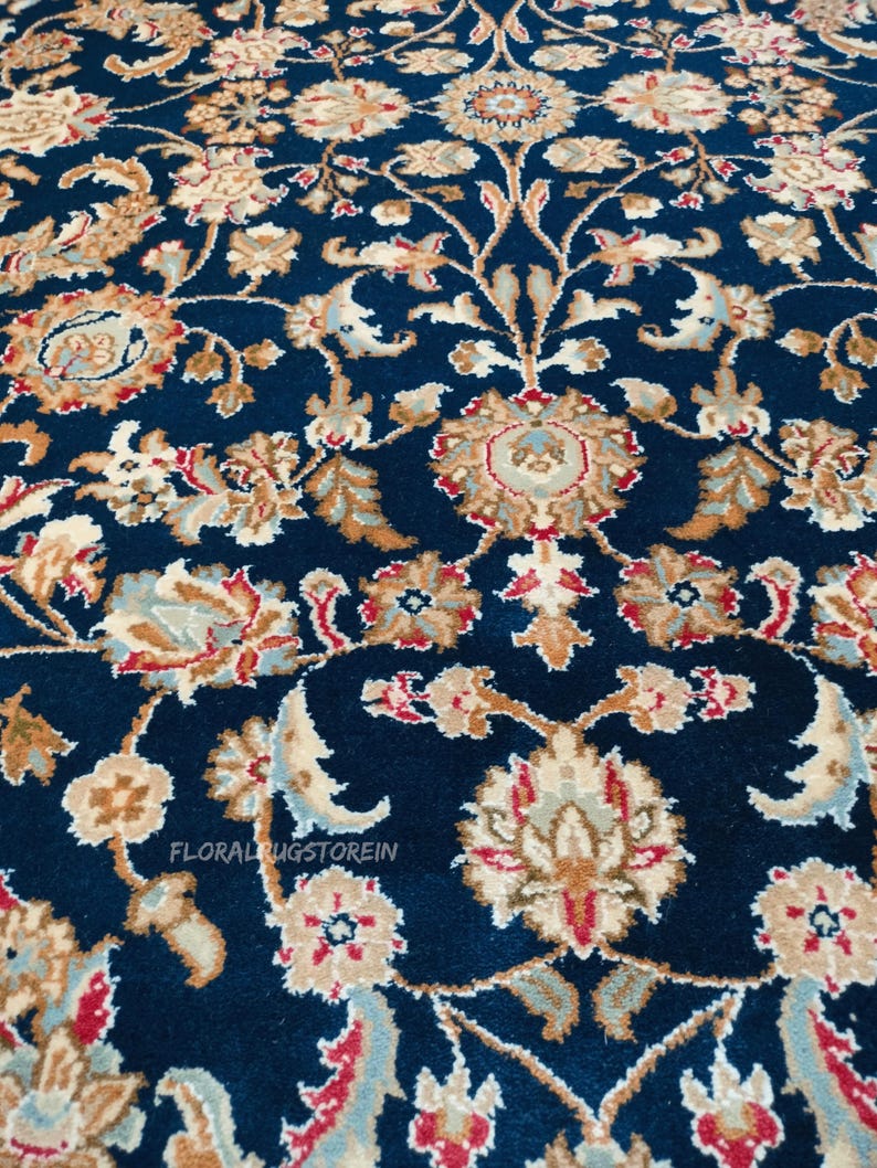 May include: Close-up of a navy blue rug with an intricate floral pattern. The design features beige, red, and light blue floral motifs and scrolling vines. The text "FLORALRUGSTOREIN" is visible.