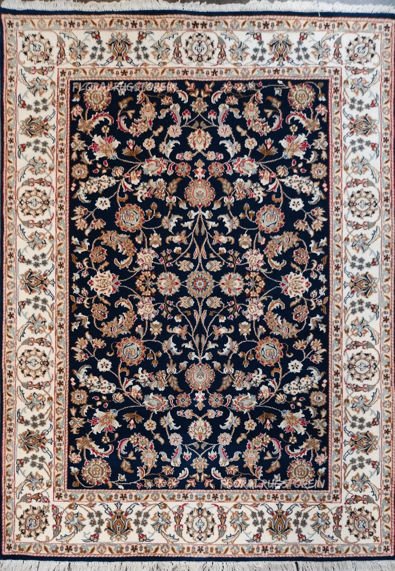 May include: A rectangular area rug with a navy blue field, featuring a dense floral pattern in shades of beige, brown, and red. The rug has a cream-colored border with intricate floral and geometric designs. The rug's edges are finished with a dark blue border and fringe.